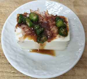 A serving of Hiyayakko, Japanese chilled tofu, topped with sliced okra, bonito flakes, and soy sauce.