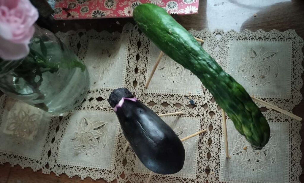 Cucumber horse and eggplant cow spirit animals for Obon, placed near a Buddhist altar and family photos.