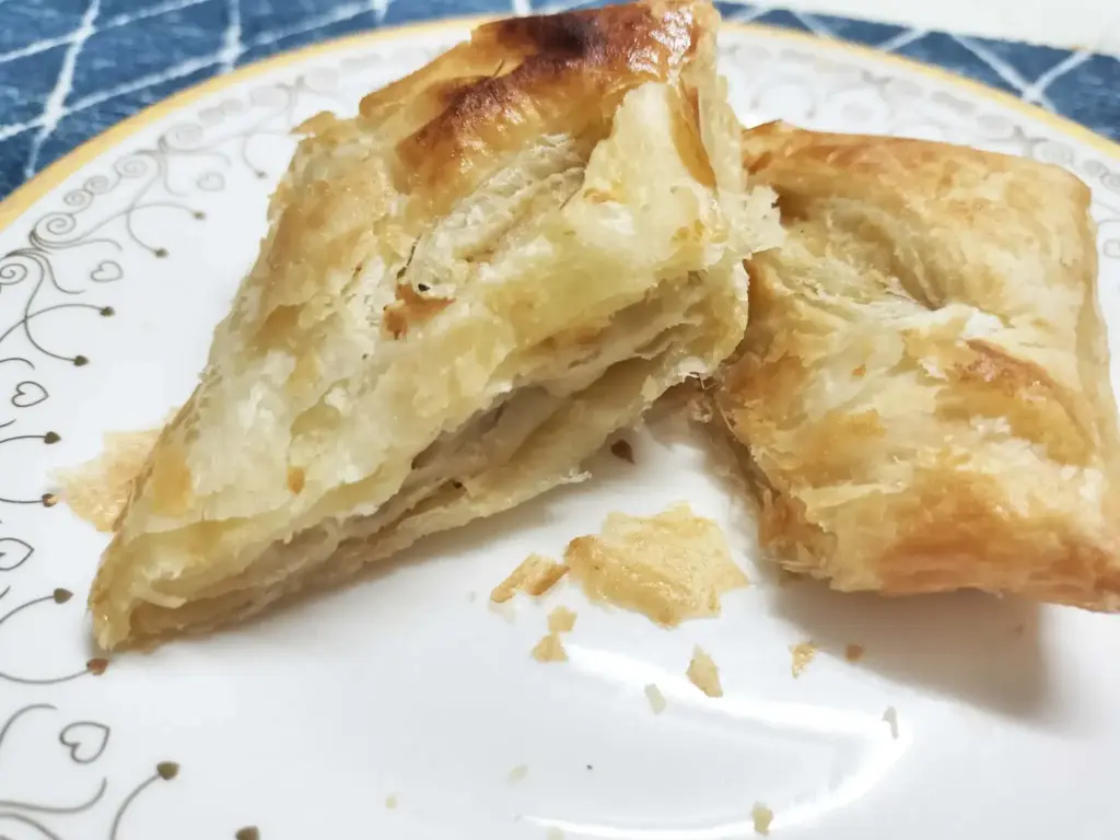 Golden flaky pastry cut in half showing its crispy layers on a decorative plate.