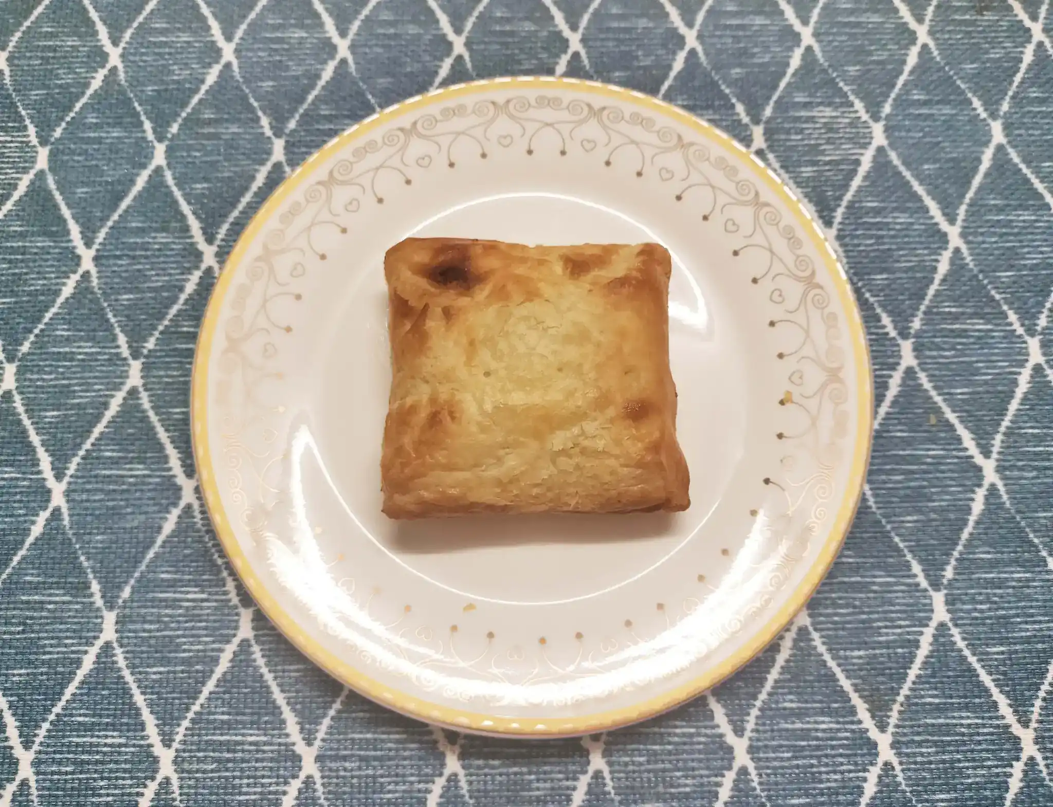 Square golden-brown pastry placed neatly on a decorative white plate with a blue patterned cloth background.