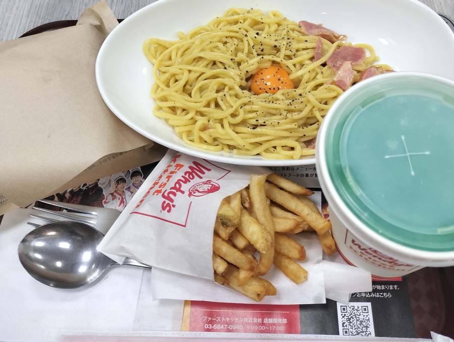 A Wendy’s First Kitchen meal in Japan featuring carbonara pasta topped with egg yolk, fries, a drink, and a wrapped burger on a tray.