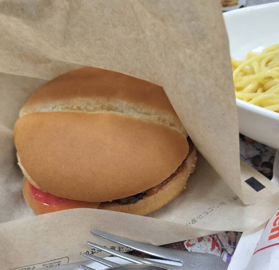 A close-up of a Wendy’s First Kitchen chili burger wrapped in paper, served with pasta on the side in Japan.